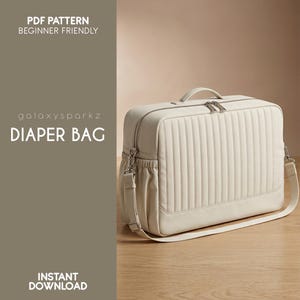 May include: Cream-coloured diaper bag with vertical quilted design, top handle, and shoulder strap. The bag has a zipped closure and side pockets. Text on the image reads "PDF Pattern Beginner Friendly", "galaxysparkz", "DIAPER BAG", and "INSTANT DOWNLOAD".