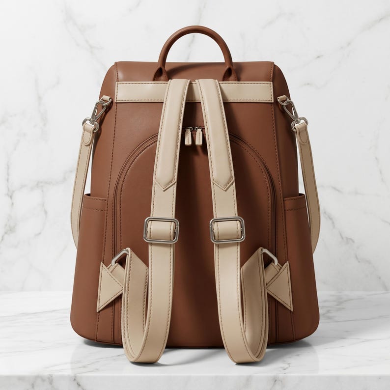 May include: Brown and beige backpack with adjustable straps and silver-tone hardware. The backpack features a top handle, two side pockets, and a front flap closure. The straps are beige, and the body is brown.
