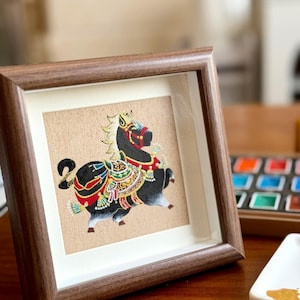 Könnte beinhalten: Gerahmtes Kunstwerk mit einem stilisierten schwarzen Pferd mit farbenfrohen Verzierungen. Das Pferd ist auf einem beigen Hintergrund in Bewegung dargestellt, eingerahmt in einem braunen Holzrahmen. Das Kunstwerk steht auf einer Holzoberfläche.