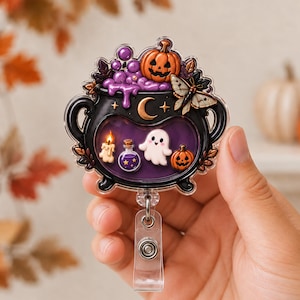May include: A black cauldron badge reel featuring a purple liquid interior with a white ghost, a small orange pumpkin, a lit candle, and a potion bottle. The top of the cauldron is decorated with a larger orange pumpkin, purple bubbles, and a moth.