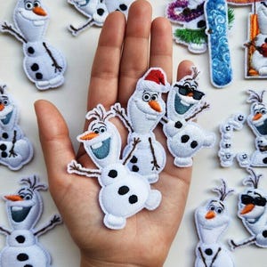 May include: A collection of white snowman patches with black button accents, carrot noses, and twig arms. Some snowmen wear sunglasses, a Santa hat, or hold a surfboard. These embroidered patches are perfect for adding to clothing or accessories.