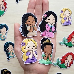 May include: A collection of embroidered patches featuring cartoon princesses. The patches showcase various princesses with different skin tones, hair colors, and outfits. Some patches have mermaid tails. The patches are colorful and detailed.