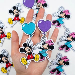 May include: A collection of embroidered patches featuring Mickey and Minnie Mouse characters. Mickey is in red shorts and yellow shoes, Minnie in a blue dress and pink bow. Some patches hold heart-shaped balloons in blue and purple.