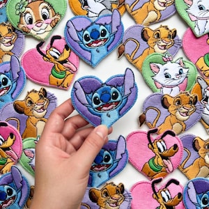 Może przedstawiać: Haftowane naszywki w kształcie serca z r&oacute;żnymi postaciami z kresk&oacute;wek, w tym Stitch, Simba, Pluto i Marie. Naszywki są w żywych kolorach i nadają się do odzieży lub akcesori&oacute;w.