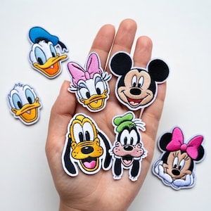 以下が含まれることがあります： 人気漫画のキャラクターが刺繍されたワッペンコレクション。ミッキーマウス、ミニーマウス、ドナルドダック、デイジーダック、グーフィー、プルートのワッペンが含まれています。各ワッペンは白い縁取りと鮮やかな色をしています。