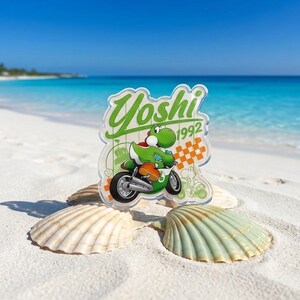 Peut inclure: Un porte-cl&eacute; en acrylique transparent repr&eacute;sentant le personnage Yoshi vert sur une moto. Le motif inclut le texte Yoshi et 1992 en vert, ainsi qu'un motif &agrave; damier orange. L'objet est pr&eacute;sent&eacute; devant un arri&egrave;re-plan d'oc&eacute;an bleu vif.