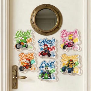 Peut inclure: Six autocollants en acrylique transparent repr&eacute;sentant les personnages de Nintendo Yoshi, Mario, Peach, Daisy, Luigi et Bowser sur leurs v&eacute;hicules. Chaque autocollant inclut le nom, l'ann&eacute;e 1992 et un motif de drapeau &agrave; damier sur une porte blanche.