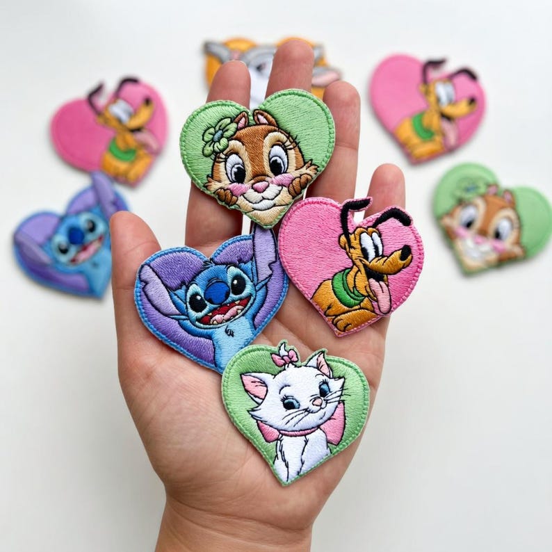 Może przedstawiać: Kolekcja haftowanych naszywek w kształcie serca z popularnymi postaciami z kresk&oacute;wek. Naszywki przedstawiają postacie takie jak Stitch, Pluto i Marie, każda na r&oacute;żowym lub zielonym sercu. Naszywki są kolorowe i szczeg&oacute;łowe, idealne do odzieży lub akcesori&oacute;w.