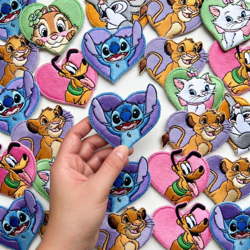 Może przedstawiać: Haftowane naszywki w kształcie serca z r&oacute;żnymi postaciami z kresk&oacute;wek, w tym Stitch, Simba, Pluto i Marie. Naszywki są w żywych kolorach i nadają się do odzieży lub akcesori&oacute;w.