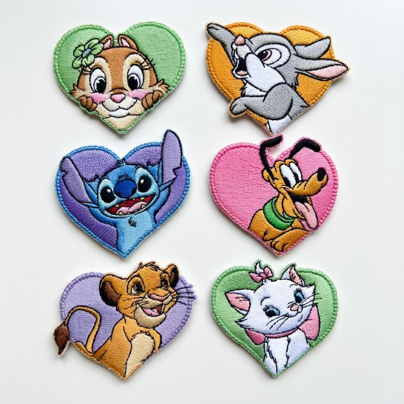 Może przedstawiać: Zestaw sześciu haftowanych naszywek w kształcie serca, przedstawiających postacie z kresk&oacute;wek. Postacie to m.in. wiewi&oacute;rka, kr&oacute;lik, Stitch, Pluto, Simba i Marie. Każda naszywka ma kolorową obw&oacute;dkę w kształcie serca.