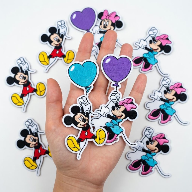 May include: A collection of embroidered patches featuring Mickey and Minnie Mouse characters. Mickey is in red shorts and yellow shoes, Minnie in a blue dress and pink bow. Some patches hold heart-shaped balloons in blue and purple.