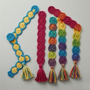 May include: Crocheted bookmarks in various colors. One is blue with yellow flowers and a yellow and blue tassel. Another is solid magenta with a magenta tassel. The others are rainbow-colored with tassels.