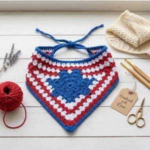 May include: A handmade crochet bandana in red, white, and blue, with a blue starburst design in the center. The bandana is tied with blue yarn. A ball of red yarn, a beige knitted hat, and a tag that says "Handmade with Love" are also visible.