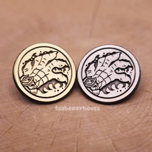 May include: Two round, metallic buttons with a detailed, stylized claw design. One button is gold-toned, the other silver-toned. The buttons are set against a wooden surface, with the text "teaberryhouse" visible.