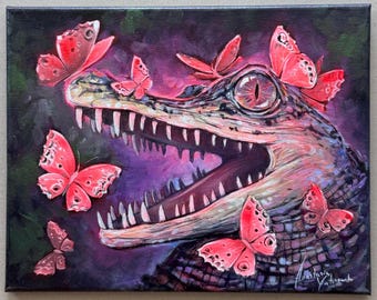 May include: A rectangular canvas painting featuring a textured, dark-scaled alligator head with an open mouth, surrounded by several vibrant pink butterflies. The background is a deep, moody purple and black, with the artist's signature in the corner.