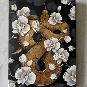 Op de afbeelding: Een rechthoekig canvas schilderij met een textuurrijke goudbruine slang die in een acht-vorm is gekronkeld tegen een zwarte achtergrond. De slang is omringd door talloze witte orchideeën met zichtbare penseelstreken en een kleine rode tong.
