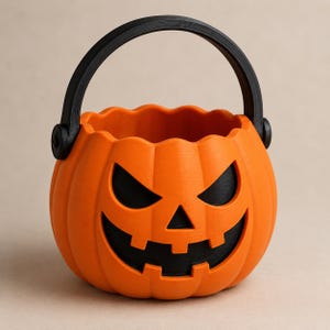 Puede incluir: Un cubo de color naranja brillante con forma de calabaza, asa negra y una cara de linterna tallada con ojos triangulares y boca dentada. El recipiente tiene un borde superior festoneado y un acabado mate suave en todo el objeto.