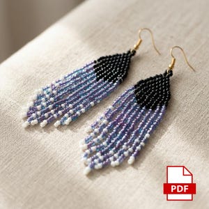 Peut inclure: Une paire de boucles d'oreilles à franges perlées. Les boucles d'oreilles présentent un haut noir, passant à des nuances de violet et de bleu, avec des accents blancs en bas. Les boucles d'oreilles ont des crochets dorés.