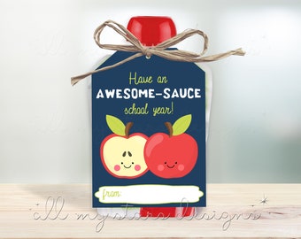 以下が含まれることがあります： 赤いリンゴと「Have an AWESOME-SAUCE school year!」という文字が書かれた青と白のギフトタグ。タグは紐で結ばれており、ギフトに付ける準備ができています。