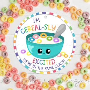Puede incluir: Una etiqueta redonda blanca con un borde colorido. La etiqueta presenta un tazón de cereal de dibujos animados con una cara sonriente y el texto "I'm Cereal-sly Excited We're in the Same Class!"