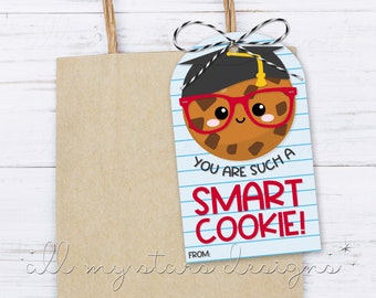May include: A blue and white printable gift tag with a brown chocolate chip cookie wearing a graduation cap and red glasses. The text on the tag reads "You are such a SMART COOKIE!" with a line for "FROM:"