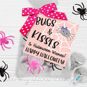 May include: A clear cellophane bag filled with candies, tied with a pink polka dot ribbon. A pink tag reads "Bugs & Kisses & Halloween Wishes! HAPPY HALLOWEEN!" with a spider web and cartoon spider. Plastic spiders in pink and black are scattered around.