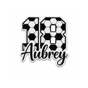 May include: A white patch with the number 18 in a soccer ball pattern, with the name "Aubrey" in a black script font. The patch has a white border and is likely for a sports uniform or personalized item.