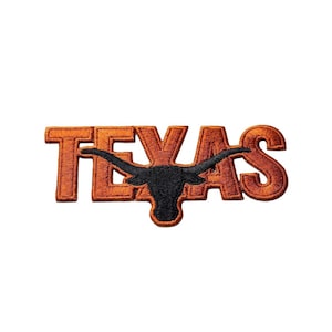 Puede incluir: Parche bordado naranja con la palabra "TEXAS" y una silueta de longhorn negra. El parche tiene un acabado texturizado, adecuado para aplicar en ropa o accesorios. El diseño está sobre un fondo blanco.