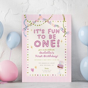 Könnte beinhalten: Eine rechteckige Geburtstagseinladungskarte mit einem rosa-weiß gestreiften Rand, dem Text IT'S FUN TO BE ONE! Isabella's First Birthday, einer kleinen Kuchenillustration und bunten Konfetti-Akzenten, umgeben von pastellfarbenen Luftballons.