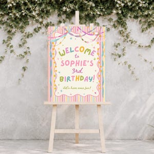 Könnte beinhalten: Ein rechteckiges Geburtstag-Willkommensschild auf einer Holzstaffelei mit cremefarbenem Zentrum und dem Text "WELCOME to SOPHIE'S 3rd BIRTHDAY! Let's have some fun!", umgeben von bunten Streifen, Luftschlangen und kleinen Sternakzenten.