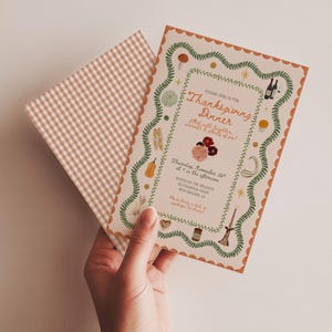 May include: A Thanksgiving dinner invitation card with a scalloped orange border and green vine illustrations, featuring text that reads Please join us for Thanksgiving Dinner, Thursday, November 26th, and a matching beige gingham envelope.