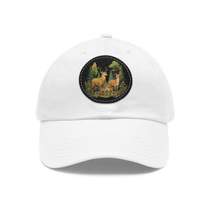 Può includere: Un cappellino da baseball bianco con una toppa circolare sul davanti. La toppa mostra un'illustrazione dettagliata di una famiglia di cervi, tra cui un cervo, una cerva e un cerbiatto, in una foresta verde con alberi e felci.