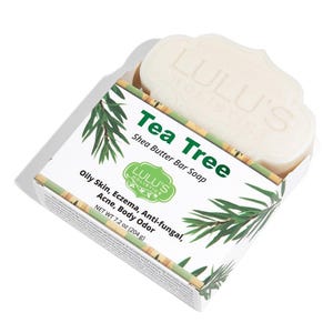 Puede incluir: Una pastilla de jabón de manteca de karité y árbol de té blanco en una caja. La caja es blanca con detalles verdes y el texto "Tea Tree" y "Lulu's Holistics". El jabón es para pieles grasas, eccemas, acné y olor corporal. Peso neto 204 g.