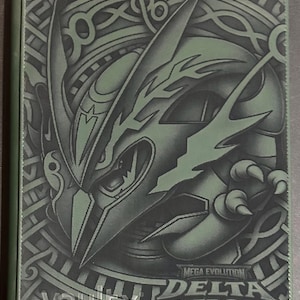 May include: A rectangular trading card binder in shades of olive green and black. The cover features a stylized creature illustration with sharp angular lines, surrounded by circular patterns. Text reads Mega Evolution Delta Reign and vaultx.