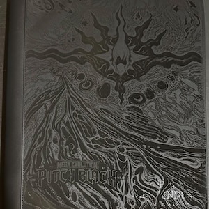 May include: A black trading card binder featuring a dark, intricate embossed design of a central star-like figure surrounded by flowing, abstract patterns. The text "MEGA EVOLUTION" and "PITCH BLACK" is printed in a bold, stylized font on the front cover.