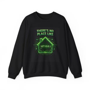 Op de afbeelding: Zwart sweatshirt met een groene afbeelding van een huis en de tekst "THERE'S NO PLACE LIKE" erboven. De huisafbeelding bevat het IP-adres "127.0.0.1". Een casual, comfortabele stijl.