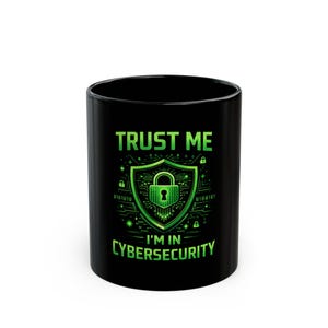 May include: Black ceramic mug with the text "TRUST ME I'M IN CYBERSECURITY" in green. The design features a green shield with a padlock and binary code details. A coffee mug for cybersecurity professionals.