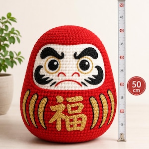 Könnte beinhalten: Handgefertigte rote Daruma-Puppe, ca. 50 cm hoch, mit weißem Gesicht und schwarzen Gesichtszügen. Die Puppe hat goldgestickte Kanji-Zeichen und ist ein traditioneller japanischer Glücksbringer.