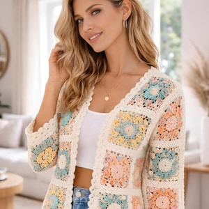 May include: Cream-colored crochet cardigan with a V-neck and three-quarter sleeves. The cardigan features square panels in pastel colors, including blue, yellow, and pink. The edges are scalloped, adding a decorative touch to the garment.
