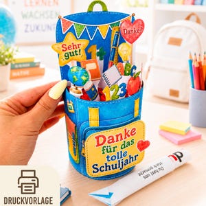 May include: A 3D pop-up greeting card shaped like a blue backpack, featuring school-themed cutouts including a globe, a red apple, a lightbulb, and the German text 'Danke für das tolle Schuljahr', 'Sehr gut!', 'Danke!', and '123'.