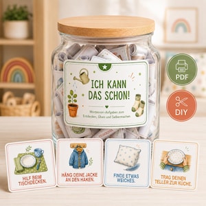 Könnte beinhalten: Ein durchsichtiges Glas mit Holzdeckel gefüllt mit gerollten Papierstreifen. Das Etikett trägt die Aufschrift ICH KANN DAS SCHON! Montessori-Aufgaben zum Entdecken, Üben und Selbermachen. Vier quadratische Karten zeigen Illustrationen und deutsche Aufgabentexte.