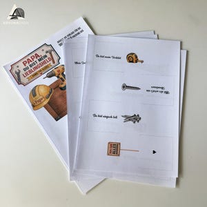 K&ouml;nnte beinhalten: Ein Stapel wei&szlig;er Papierb&ouml;gen mit deutschem Text und Illustrationen. Ein Bogen zeigt einen Titel mit Werkzeugen und einer Holzkiste. Andere B&ouml;gen haben ein Ma&szlig;band, eine Schraube und N&auml;gel. Der Text lautet "Papa, Du bist mein Lieblingsheld."