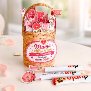 Könnte beinhalten: Ein Weidenkorb gefüllt mit Papierblumen, Herzen und Fähnchen. Ein dekoratives Etikett auf dem Korb lautet "Mama Alles Liebe zum Muttertag Danke für deine Liebe." Zwei Schokoriegel und ein Blumenschöpfer befinden sich vor dem Korb.