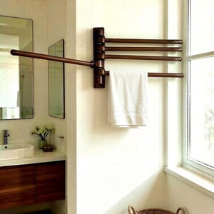 May include: A wall-mounted, dark bronze-toned towel rack featuring four horizontal, pivoting arms. One arm is extended outward, while the other three are folded against the wall. A single white towel hangs from the lowest extended arm.