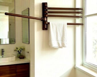 May include: A wall-mounted, dark bronze-toned towel rack featuring four horizontal, pivoting arms. One arm is extended outward, while the other three are folded against the wall. A single white towel hangs from the lowest extended arm.