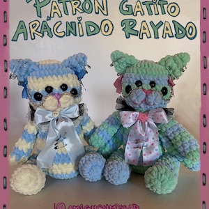 Puede incluir: Dos muñecos de gato hechos a mano con ganchillo. Uno es azul y blanco, el otro verde y azul. Ambos tienen lazos, imperdibles y ojos de botón negros. El texto "Patrón Gatito Arácnido Rayado" está en la parte superior.