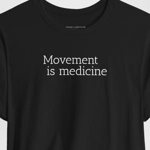 May include: Black t-shirt with the white text "Movement is medicine" across the chest. The shirt has short sleeves and a crew neck. The brand name is printed on the sleeve.