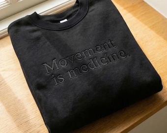 El movimiento es medicina. Sudadera negra bordada de cuello redondo para profesionales de la rehabilitación y la medicina.