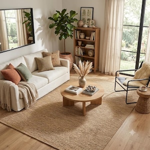 Könnte beinhalten: Ein Wohnzimmer mit einem cremefarbenen Sofa mit orangefarbenen und grünen Kissen, einem runden Couchtisch aus Holz mit einer Vase aus getrocknetem Gras, einem hohen Holzregal, einer großen Topfpflanze, einem schwarzen Metallstuhl und einem Juteteppich.
