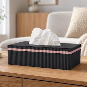 May include: A rectangular black tissue box cover with a ribbed texture and a single horizontal pink stripe running across the upper section. A white tissue is pulled through the rectangular opening at the top of the container.